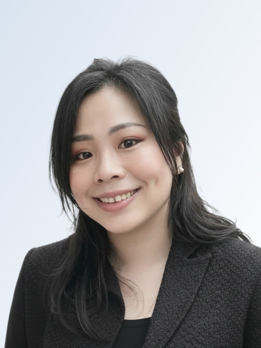Shierly Dewi, smiling, in a dark jacket against a white background